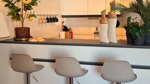 Moderni keittiö, jossa on valkoiset kaapit, ruukussa oleva sitruunapuu ja baaritiski kolmella jakkaralla.
