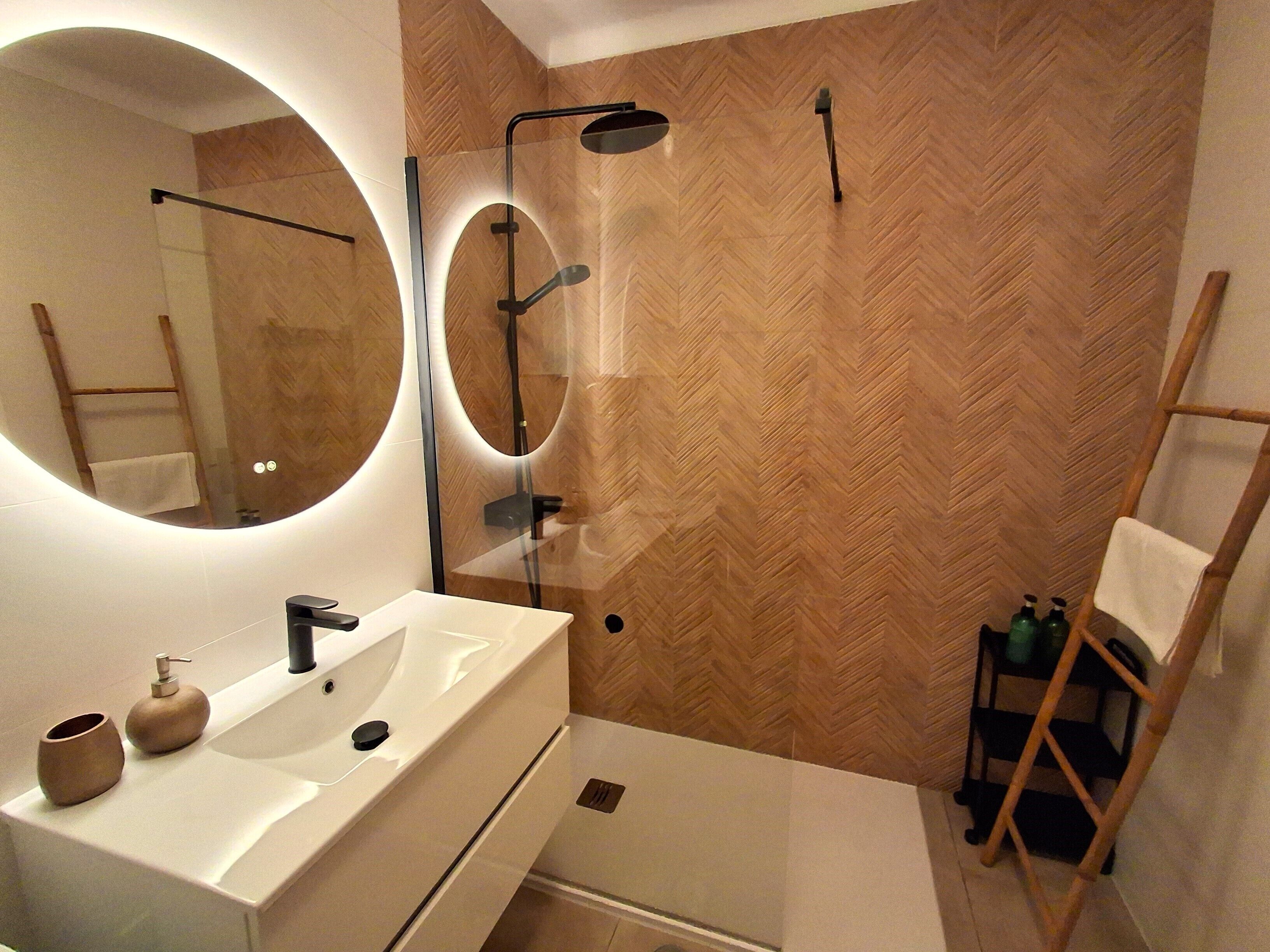 Un baño moderno con un espejo grande, un lavamanos blanco y una zona de ducha.