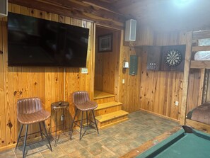 Ein Holzinterieur mit Fernseher, zwei Ledersesseln, einer Dartscheibe und einem Billardtisch.