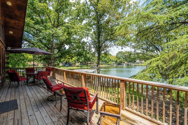 A wooden deck with red chairs and a table, overlooking a lake with boats.