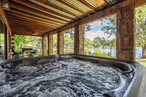 A hot tub area with a wooden ceiling and stone pillars, overlooking a lake with boats. - Luxury Log Cabin on Lake- Sleeps 14 with private boat dock & ramp (Hot Springs)