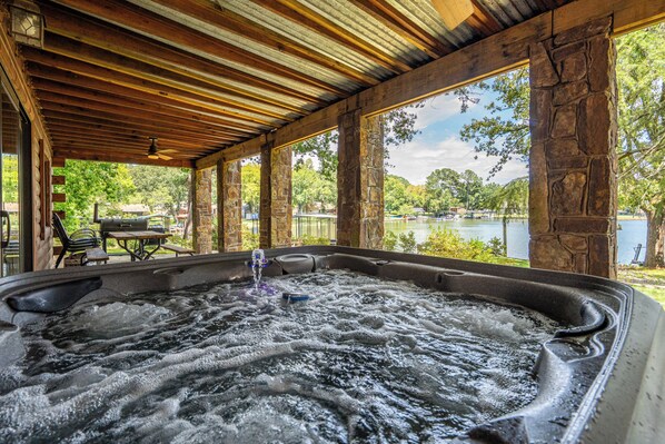 A hot tub area with a wooden ceiling and stone pillars, overlooking a lake with boats.