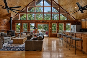 A spacious living area with a high ceiling, large windows, and a kitchen with bar stools. - Luxury Log Cabin on Lake- Sleeps 14 with private boat dock & ramp (Hot Springs)