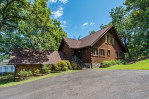A two-story log cabin with a stone foundation, a sloped roof, and a front porch.