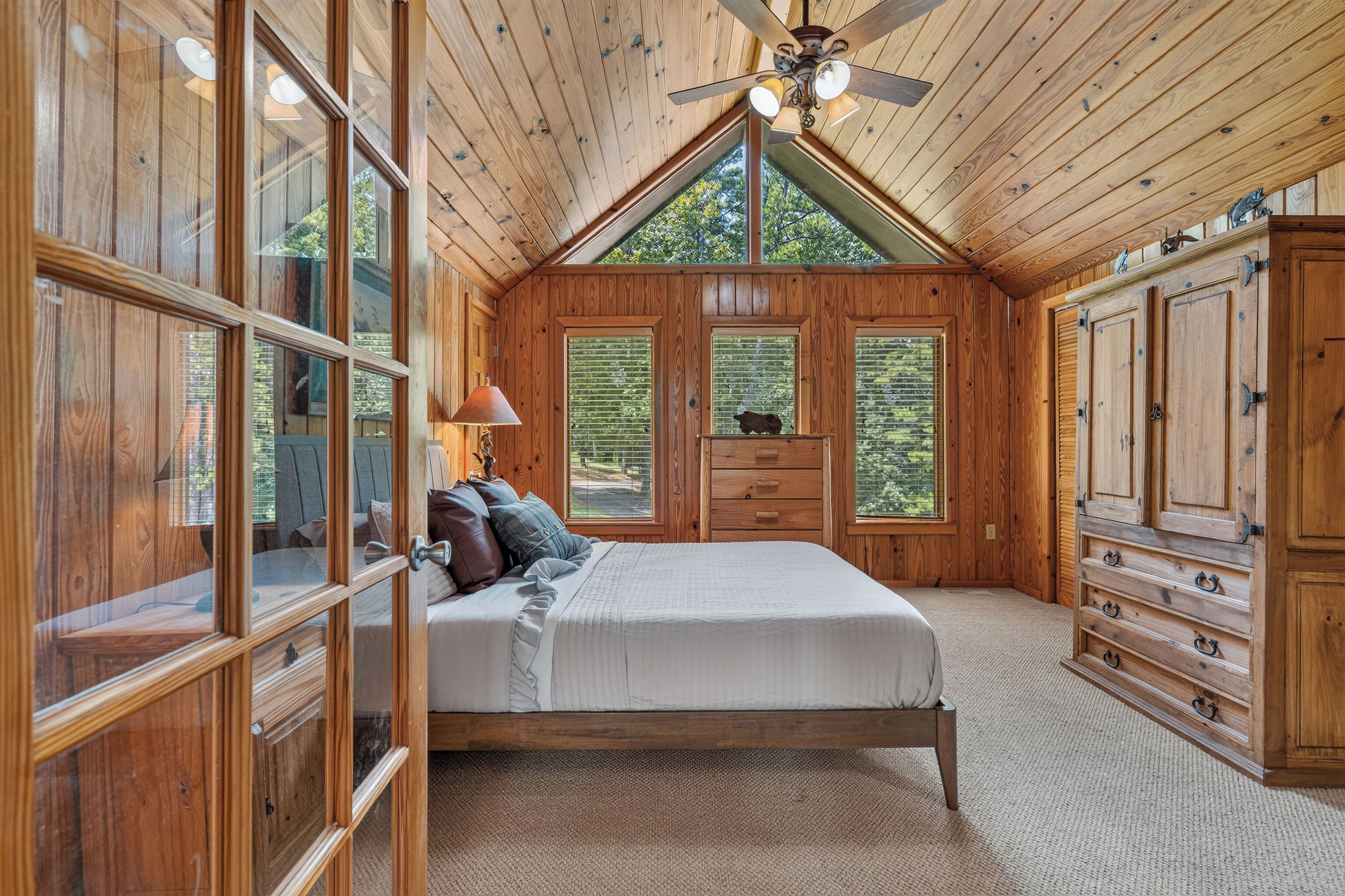 Une chambre à coucher avec un plafond en bois, un lit, une commode et une fenêtre avec des stores.