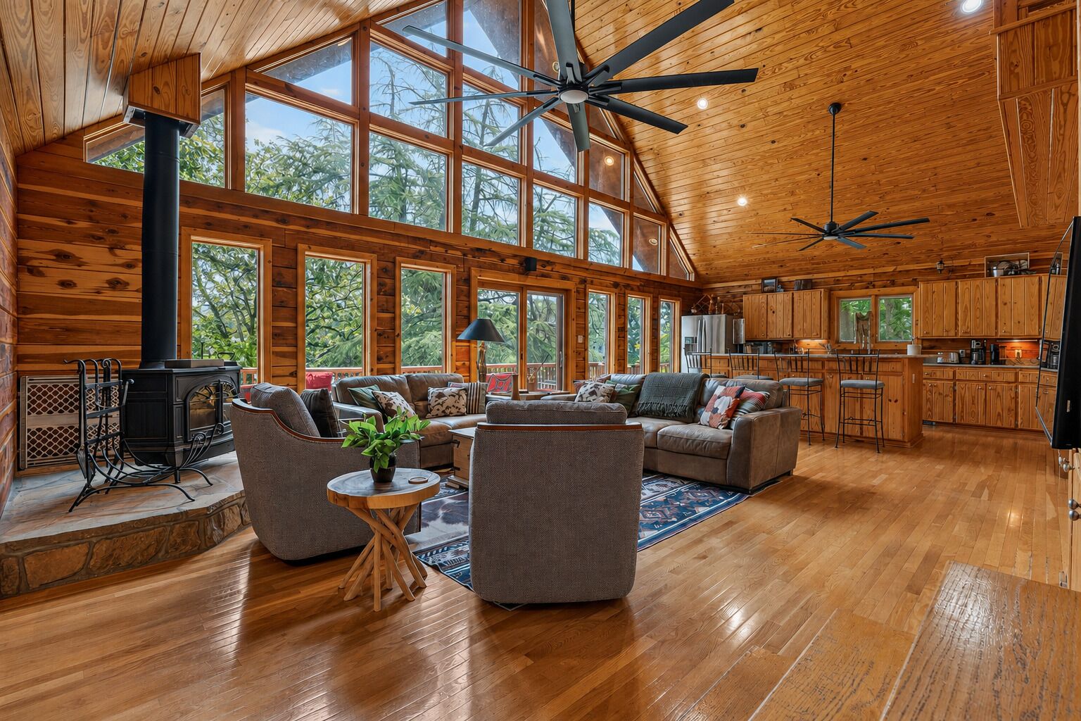 A spacious cabin interior with a large open living area, wooden floors, and a high ceiling with fans.