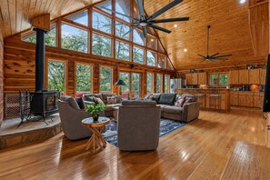 A spacious cabin interior with a large open living area, wooden floors, and a high ceiling with fans.
