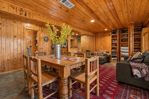 A wooden interior with a dining table, chairs, a sofa, and a bookshelf.