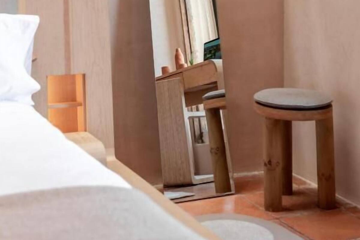 A bedroom with a bed, a wooden stool, a mirror, and a small table.