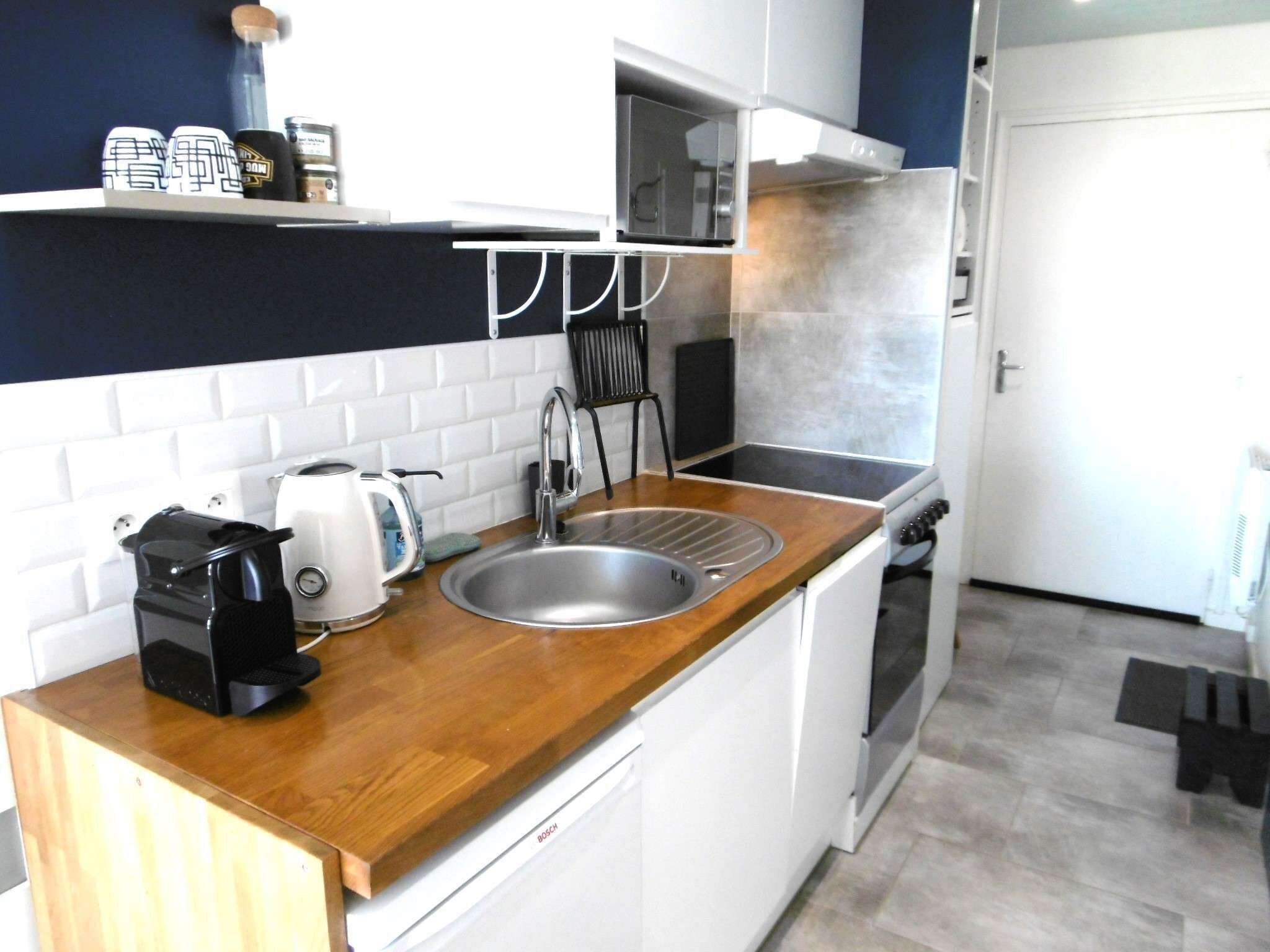 A compact kitchen with a sink, stove, and a coffee maker on the counter.