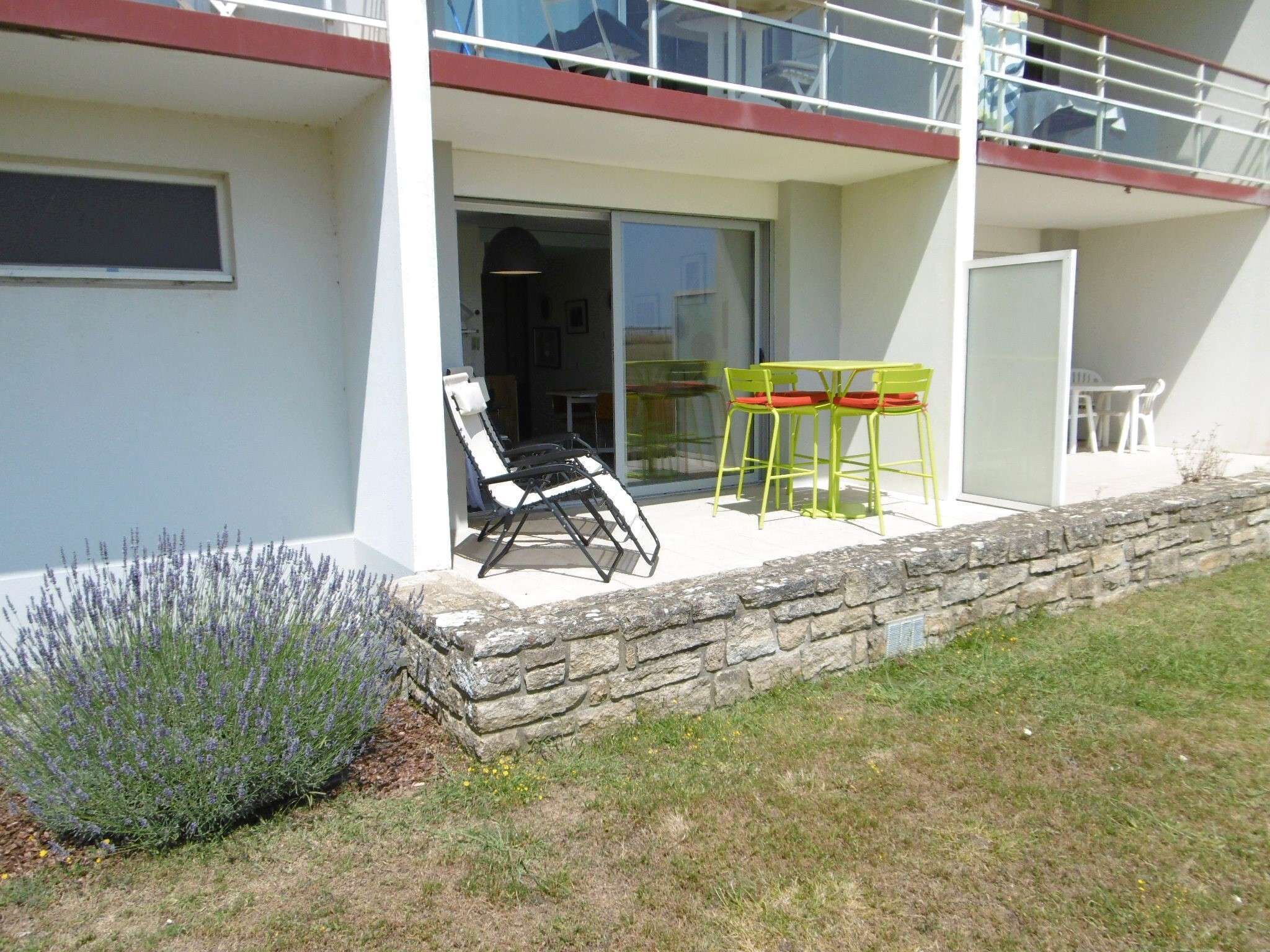 A modern building with a balcony, outdoor seating, and a stone wall.
