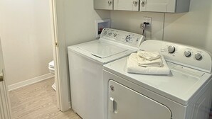 Une buanderie équipée d’un lave-linge et d’un sèche-linge, avec un plancher en bois et une porte donnant sur une autre pièce.