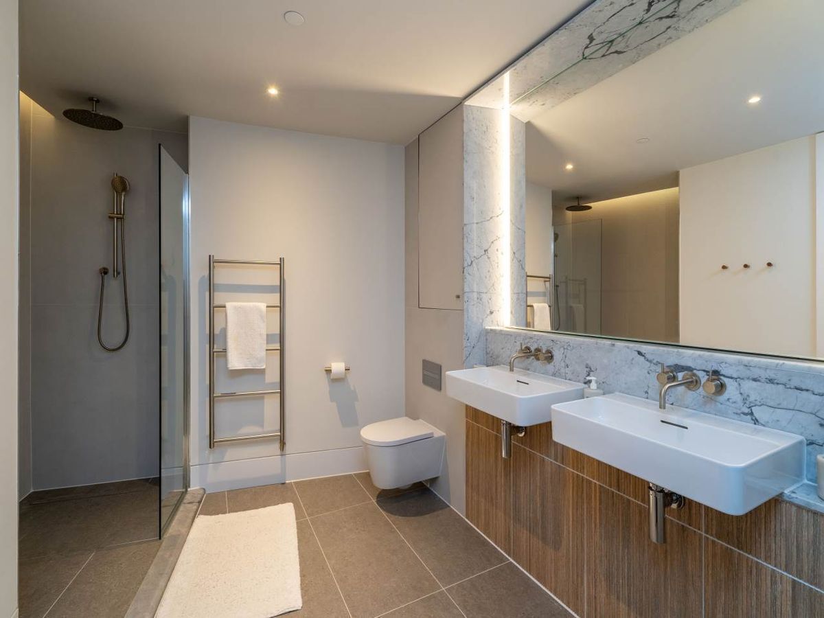 A modern bathroom with a glass shower enclosure, two sinks, a toilet, and a marble-topped vanity.