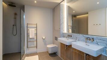 A modern bathroom with a glass shower enclosure, two sinks, a toilet, and a marble-topped vanity.