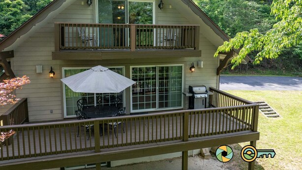 A two-story cabin with a balcony, outdoor seating, and a grill.