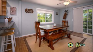A dining area with a wooden table and chairs, a ceiling fan, and a window with a view of greenery.