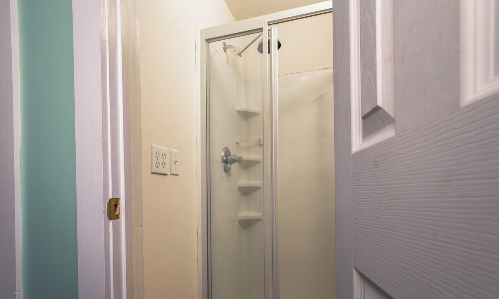 Een douche met glazen wanden en deur, een lichtschakelaar en een stopcontact op de muur.