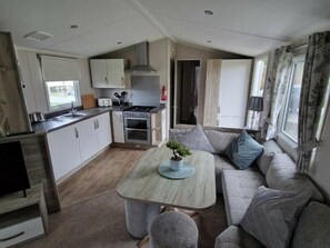 A compact kitchen with a stove, oven, and sink, a dining area with a table and chairs, and a living area with a sofa and cushions. - Southview Holiday Park - Holiday Accommodation 21279 (Skegness)