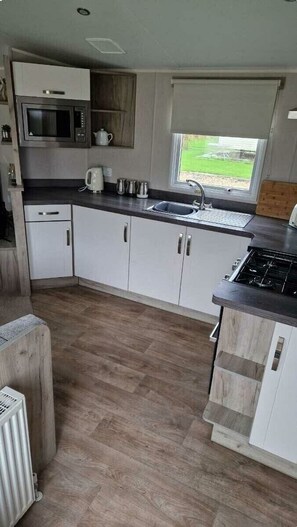 A compact kitchen with a microwave, stove, sink, and white cabinets. - Southview Holiday Park - Holiday Accommodation 21279 (Skegness)