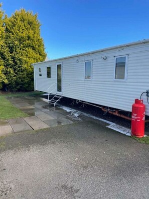 A mobile home with a front door, windows, a fire extinguisher, and a grassy area with a paved path. - Southview Holiday Park - Holiday Accommodation 21279 (Skegness)