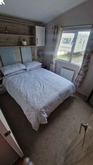 A bedroom with a bed, a wardrobe, a window with curtains, and a radiator. - Southview Holiday Park - Holiday Accommodation 21279 (Skegness)