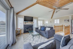 Ein geräumiges Wohnzimmer mit Kamin, großem Flachbildfernseher und Deckenventilator.