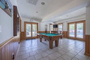 Una sala con piscina y mesa de billar, paredes de madera y ventanas amplias.