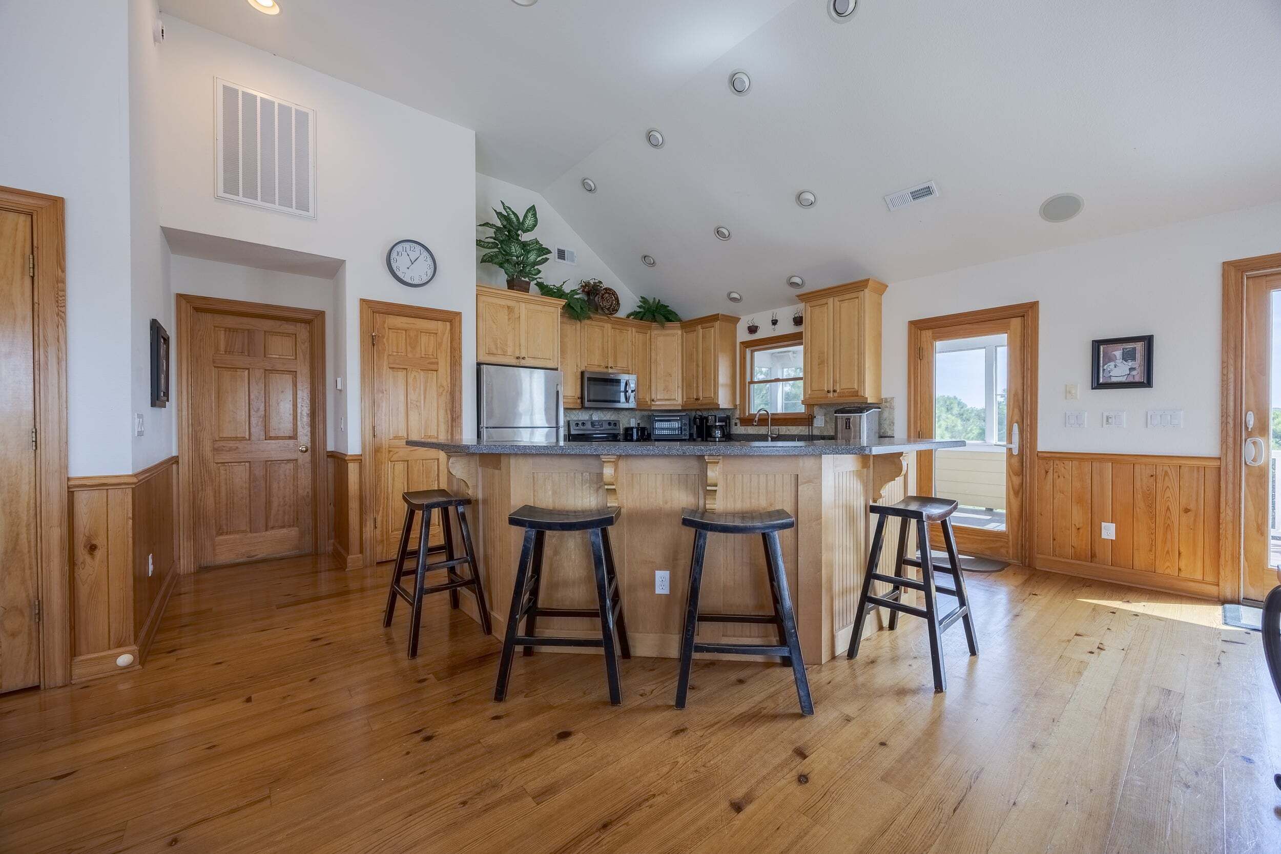 A kitchen with wooden cabinets, a central island with stools, a stainless steel refrigerator, and a microwave.