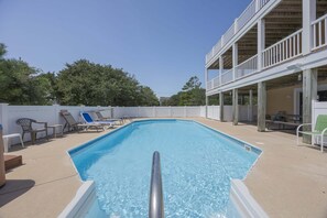 A rectangular outdoor swimming pool with a metal safety railing, surrounded by lounge chairs and a white fence. - 1925 - Lemon Cooler Your Corolla dream stay: 6BR, pool, hot tub, theater room & sunny decks. (Corolla)