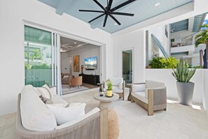 A modern living room with a ceiling fan, a sofa, a coffee table, and a large potted plant. - Olde Naples 2BR condo with pool view, heated pool, balcony, and walkable location. (Naples)