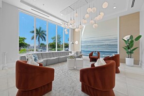 A modern living room with a large window, a sofa, two armchairs, a coffee table, and pendant lights. - Olde Naples 2BR condo with pool view, heated pool, balcony, and walkable location. (Naples)