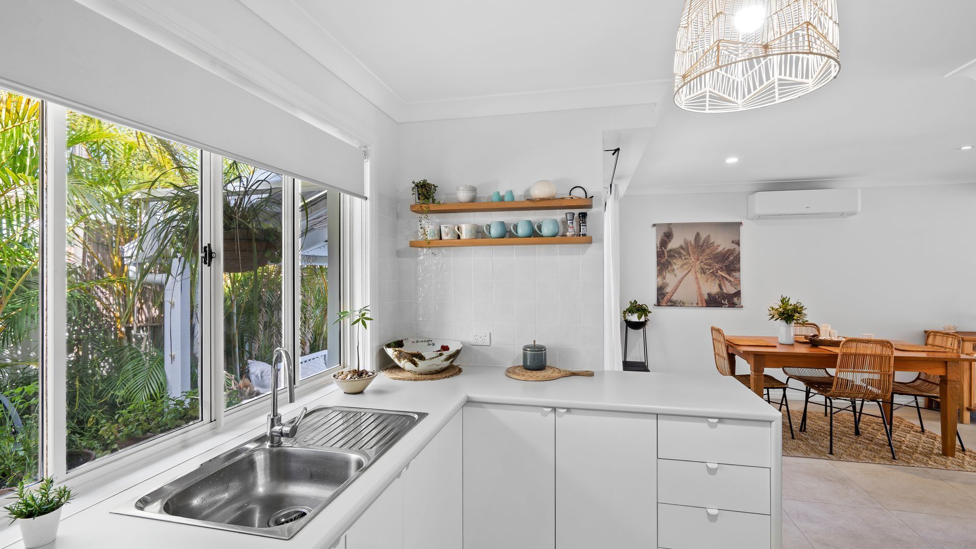 Una cocina moderna con armarios blancos, un ventanal grande y una zona de comedor con mesa y sillas de madera.