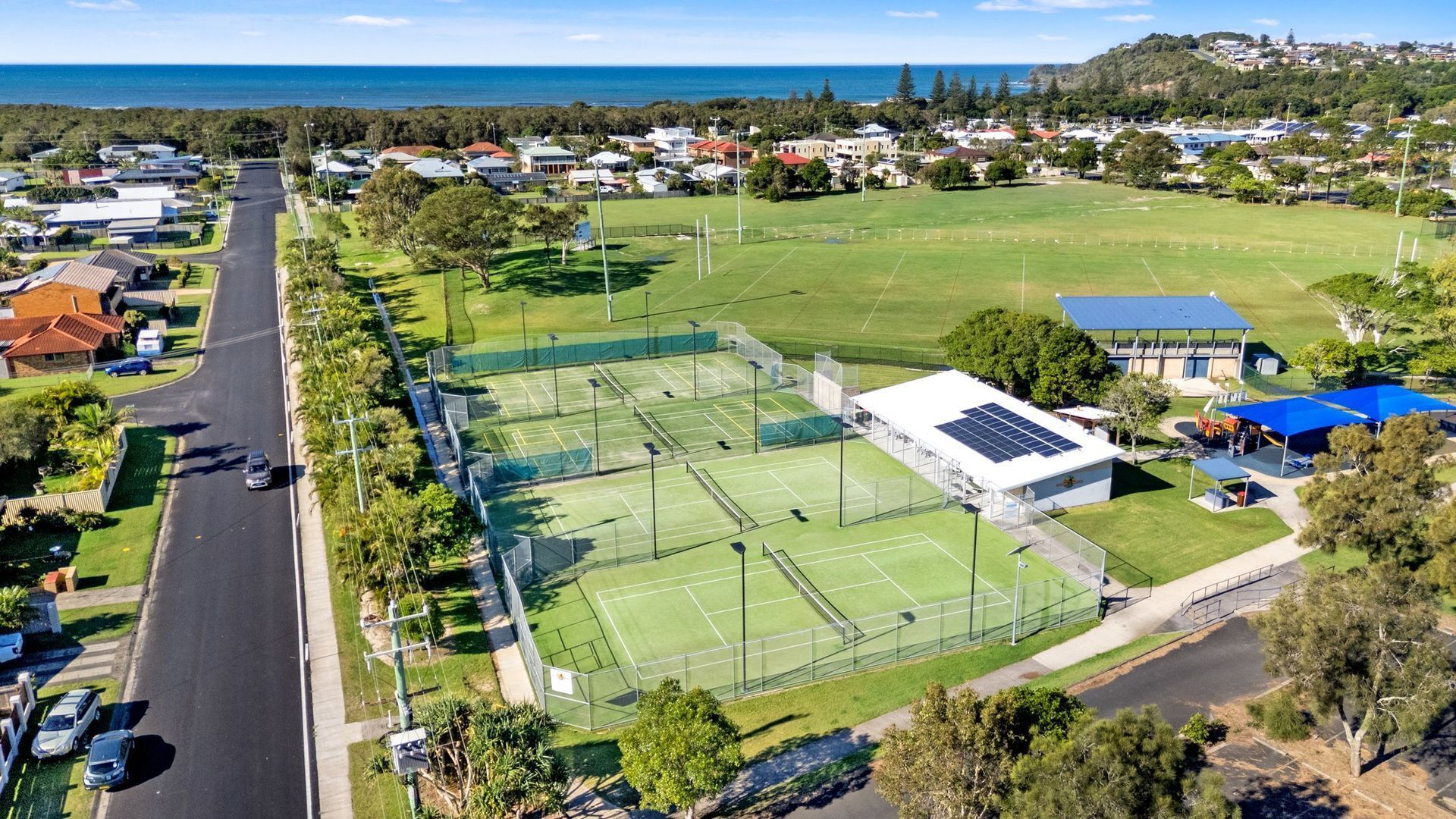Vista aérea de una zona residencial con cancha de tenis, carretera y casas.