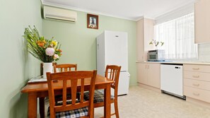 A compact kitchen with a dining table, chairs, a refrigerator, an oven, and a window with curtains. - Blue Meadow - Pet Friendly (Evans Head)