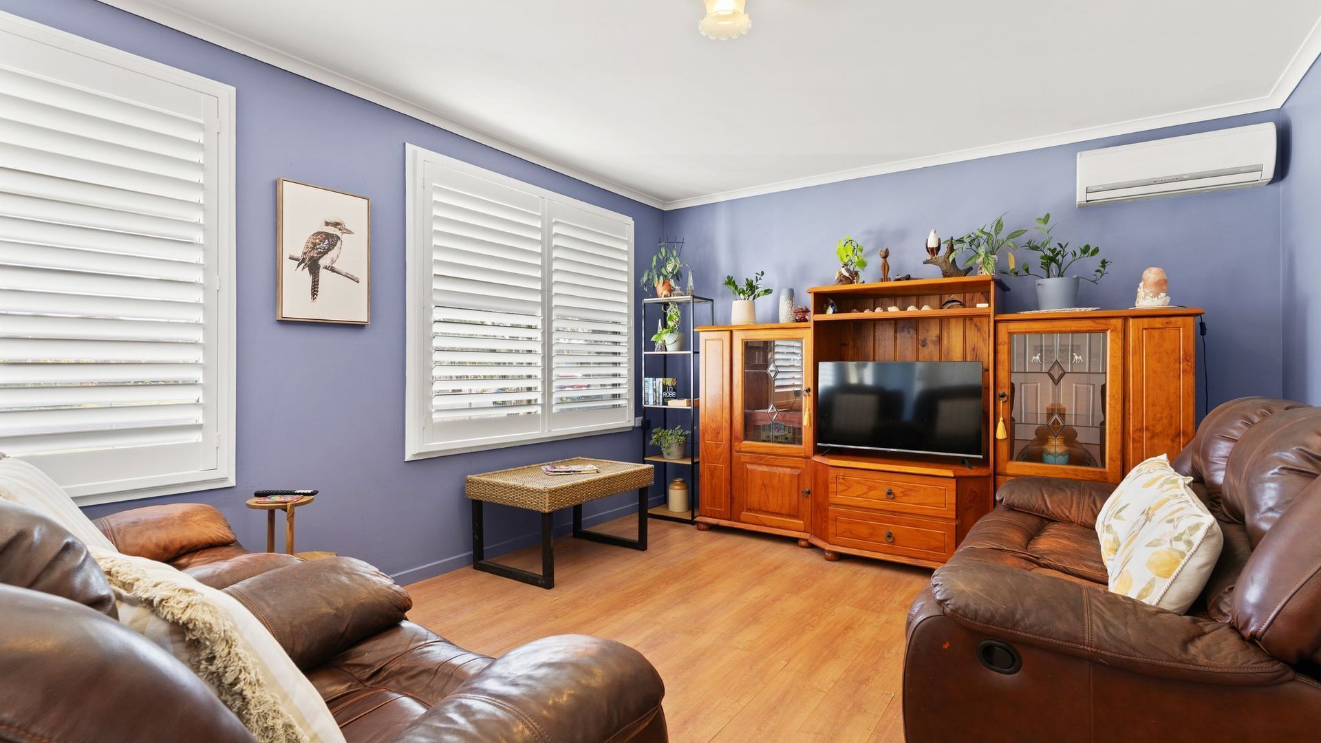 A living room with a TV, leather sofas, a wooden cabinet, and a bookshelf.