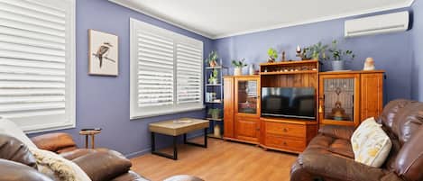 Una sala de estar con televisor, sofás de cuero, un mueble de madera y una estantería.