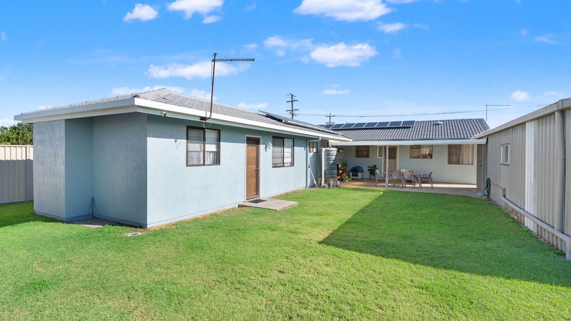 A two-story mobile home with a small backyard, a patio, and solar panels on the roof.