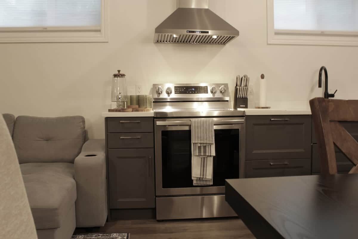 Une cuisine compacte dotée d’un four encastré, d’une hotte en acier inoxydable et d’un coin repas avec une table et des chaises en bois.