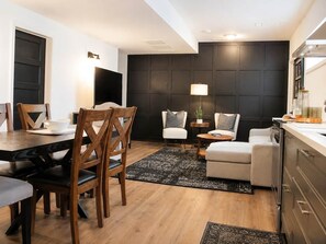 Uma sala de estar moderna com área de jantar, sofás, mesa de centro, televisão e cozinha com armários.