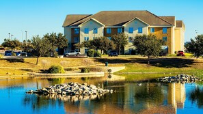 A multi-story residential building with a tiled roof, a landscaped area with trees, and a pond with rocks. - Accessible 1BR Suite w/ Breakfast Included & Pool (Laredo)