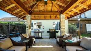 An outdoor patio with wicker furniture, a grill, and a stone pillar.