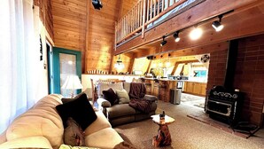 A cozy cabin interior with a living room, kitchen, and a fireplace.