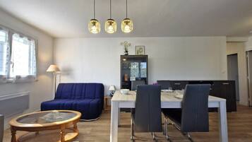 A modern living room with a sofa, a dining table, and a glass coffee table. There are three pendant lights above the table.