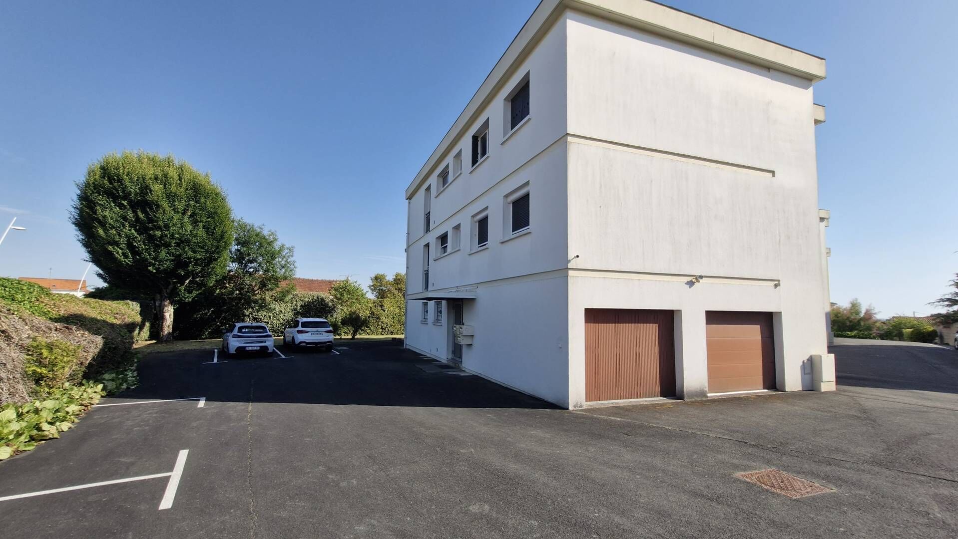 A building with a flat facade, two visible garage doors, and a parking lot with two cars.