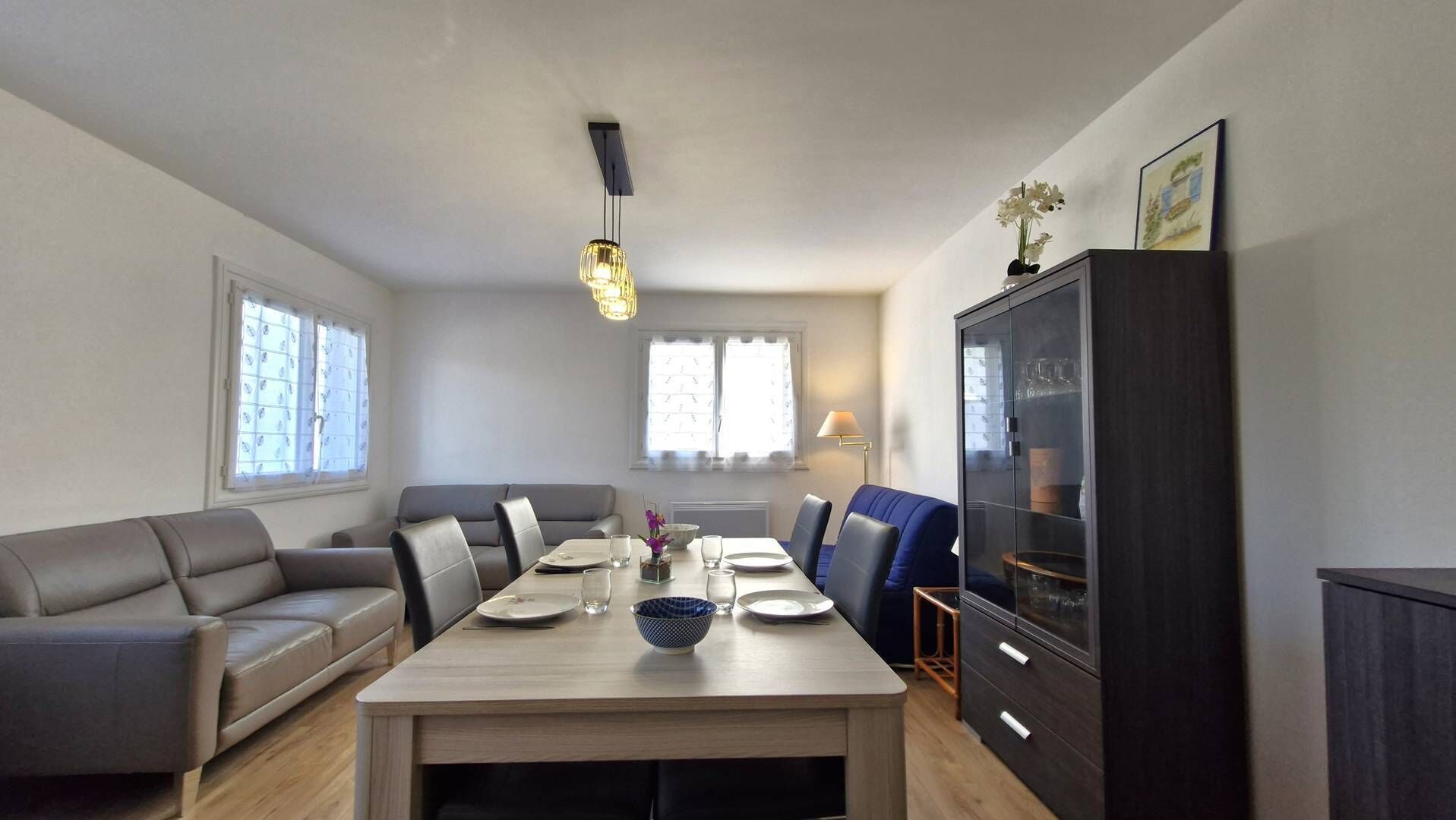 Un comedor con una mesa dispuesta para cuatro, un sofá, un armario y una ventana con persianas.