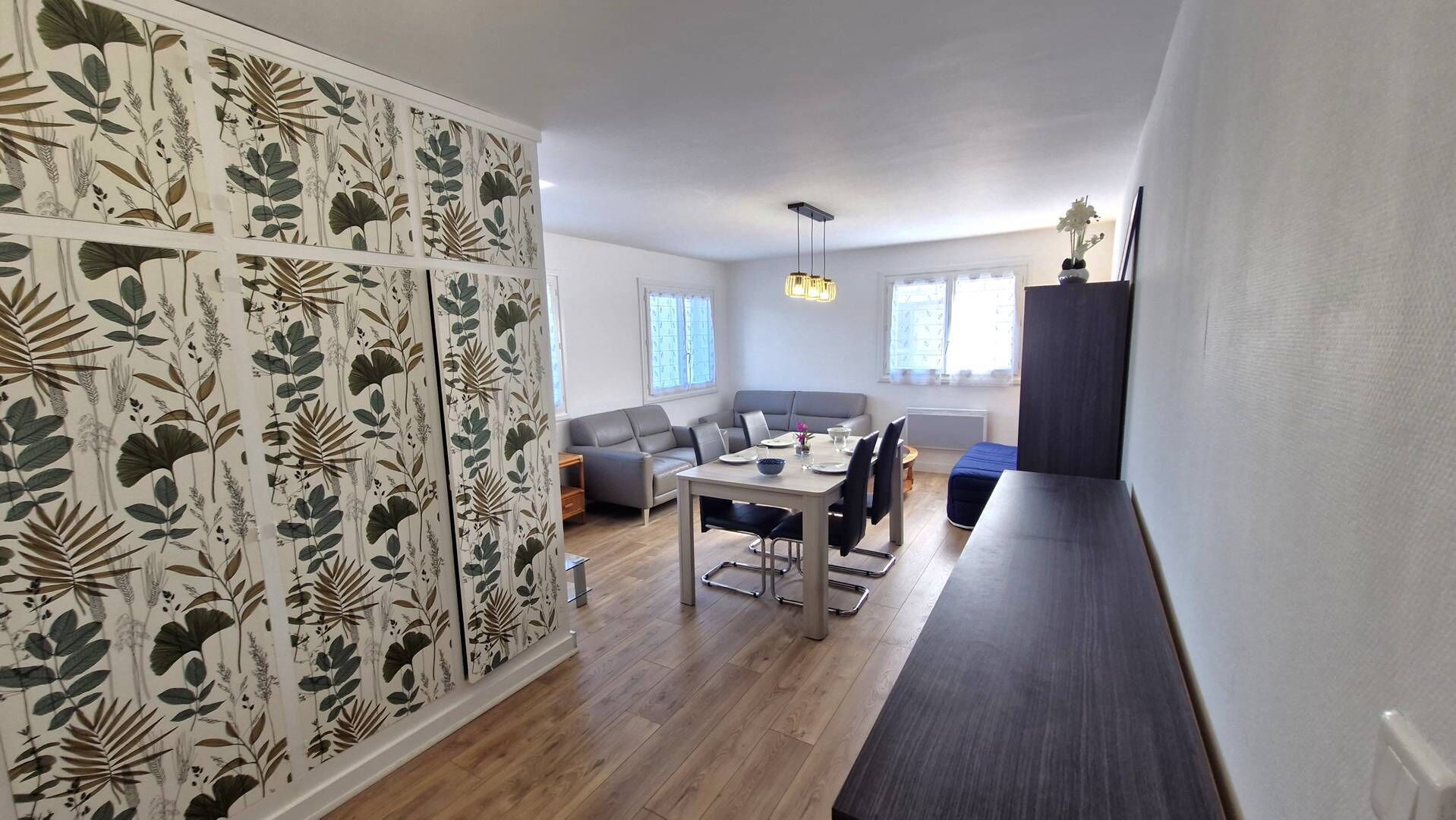 A modern living space with a dining area, a sofa, and a decorative wall with botanical prints.