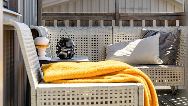 Ein Korbelementsofa mit Kissen, ein kleiner Tisch mit Lampe und eine gelbe Tagesdecke.