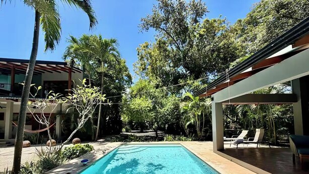 A rectangular swimming pool with clear blue water, surrounded by palm trees and a covered area with lounge chairs. - Casa Amorosa: Private Villa with Pool Near Beach & Surf Break playa grande (Playa Grande)