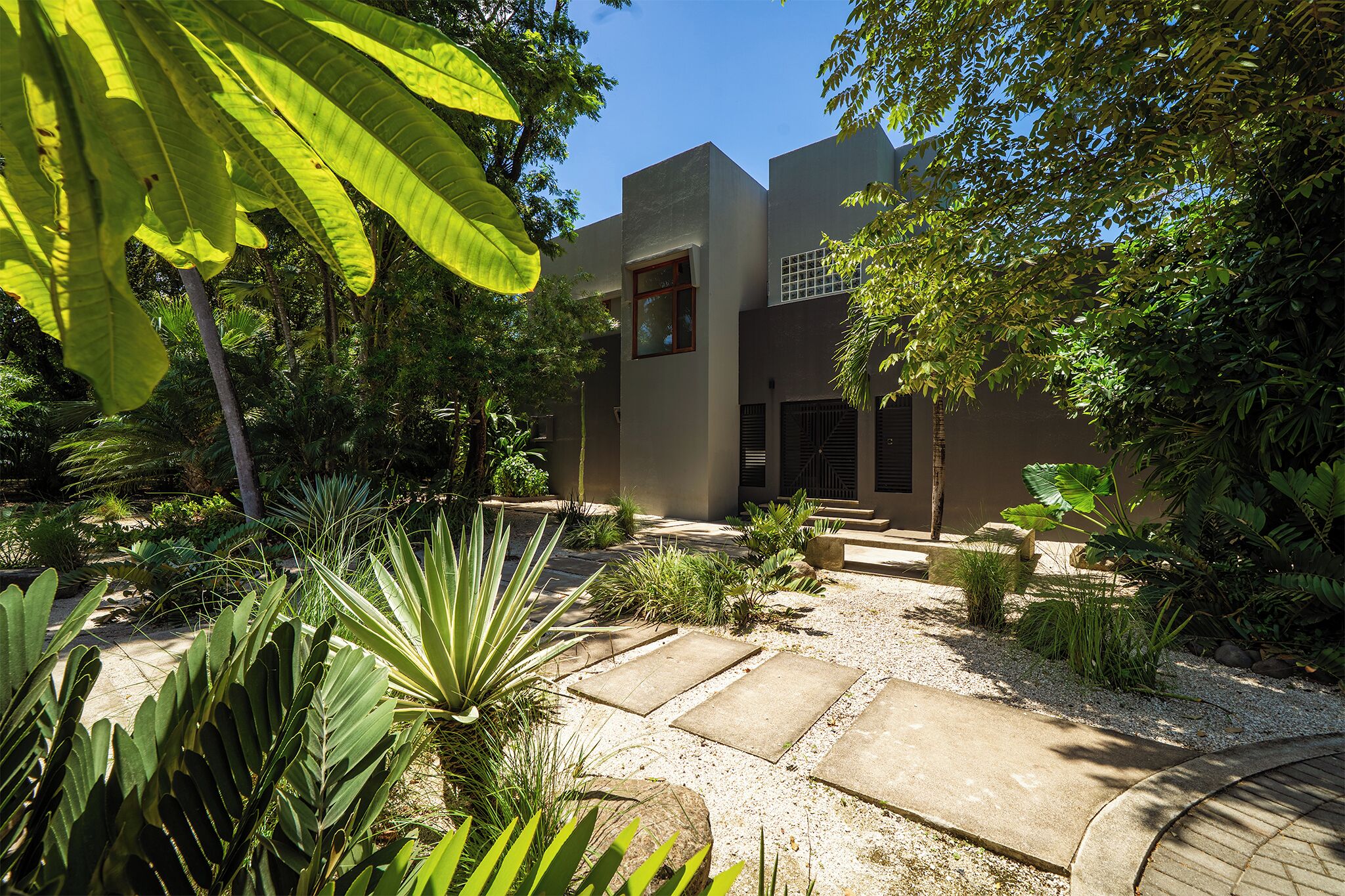 A modern building with a flat roof, surrounded by a garden with various plants and a gravel pathway.