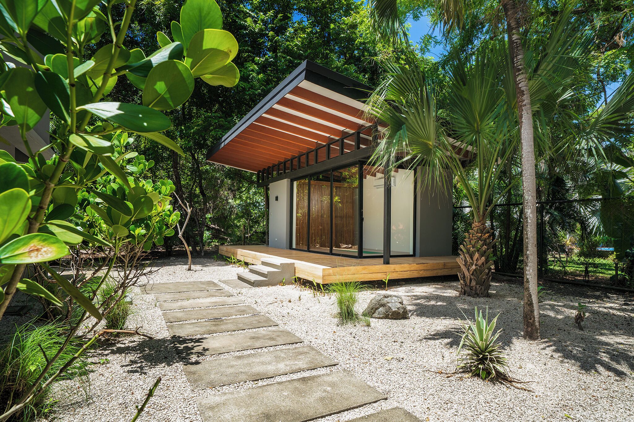 A modern house with a wooden deck, surrounded by gravel and greenery.